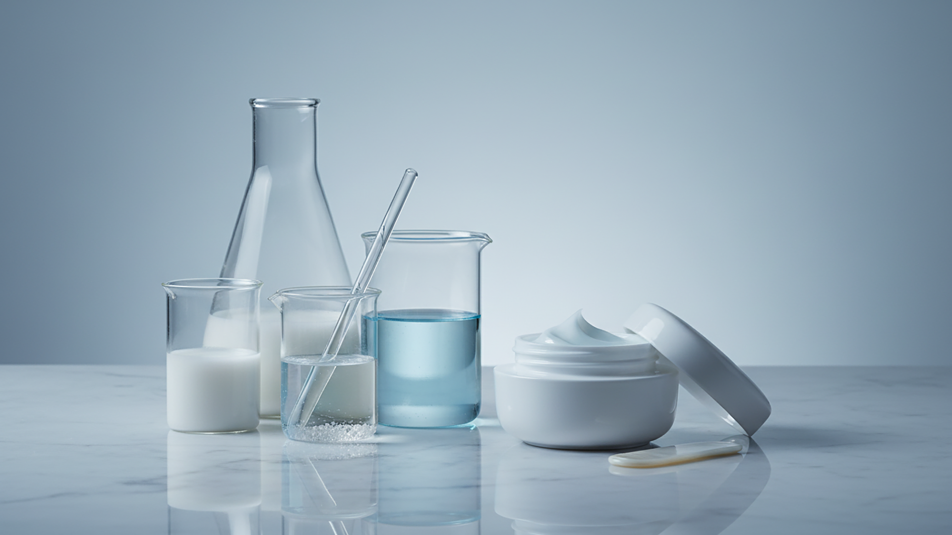 Stillleben mit transparenter Laborglasware und Kosmetikdose auf heller Fl&auml;che: Messbecher, Reagenzglas und Kolben mit wei&szlig;er und blauer Fl&uuml;ssigkeit, daneben eine ge&ouml;ffnete Creme. Ideal zur Visualisierung von Qualit&auml;tskontrolle, Inhaltsstoffpr&uuml;fung und unabh&auml;ngiger Pr&uuml;fung in regulierten Branchen.